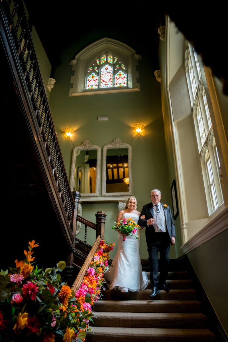 Bride walking down staircase with colourful flowers