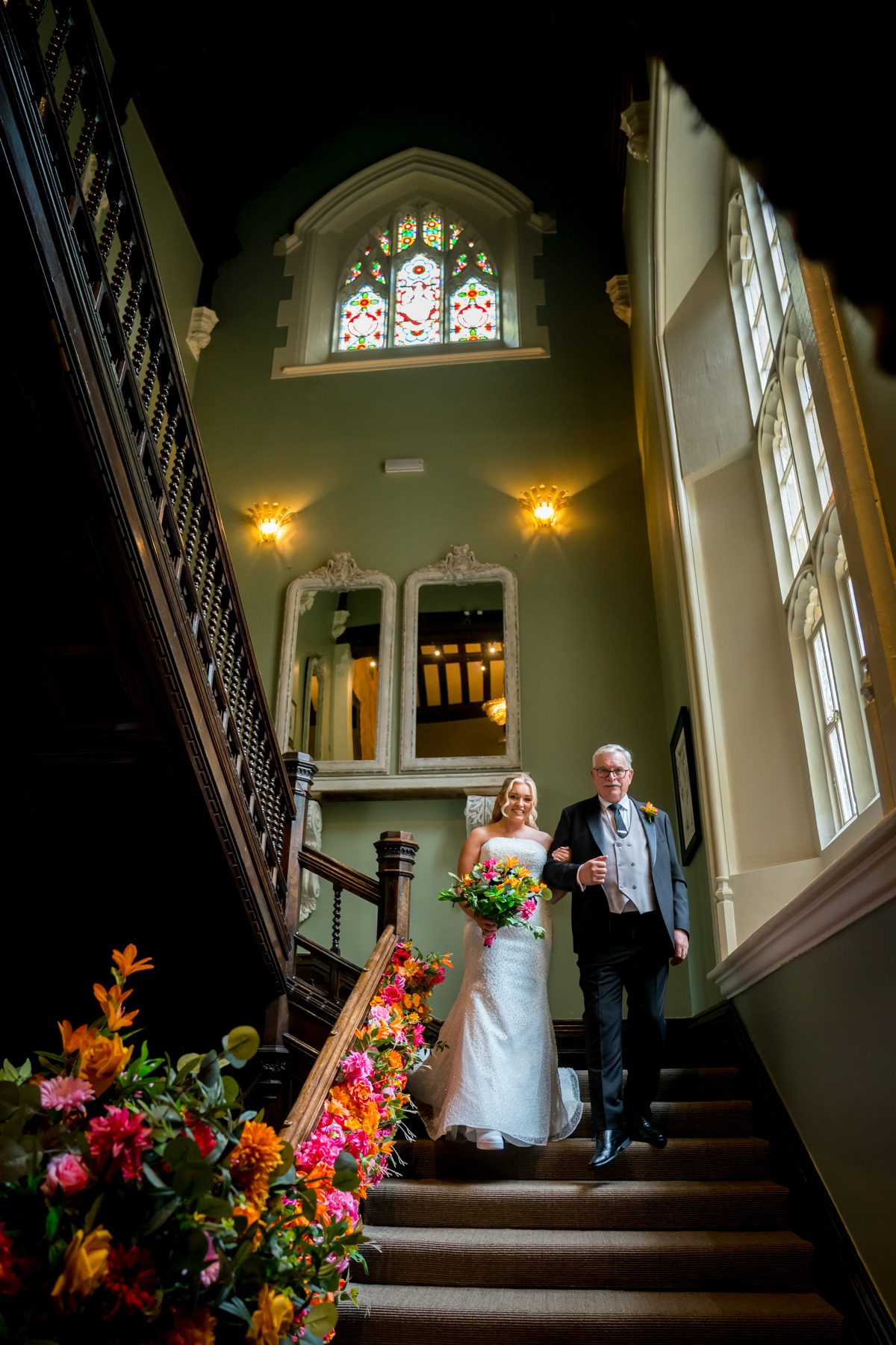 Bride walking down staircase with colourful flowers