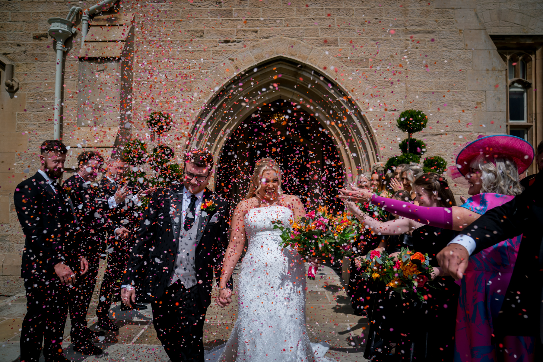 Bride and groom surrounded by colourful confetti.