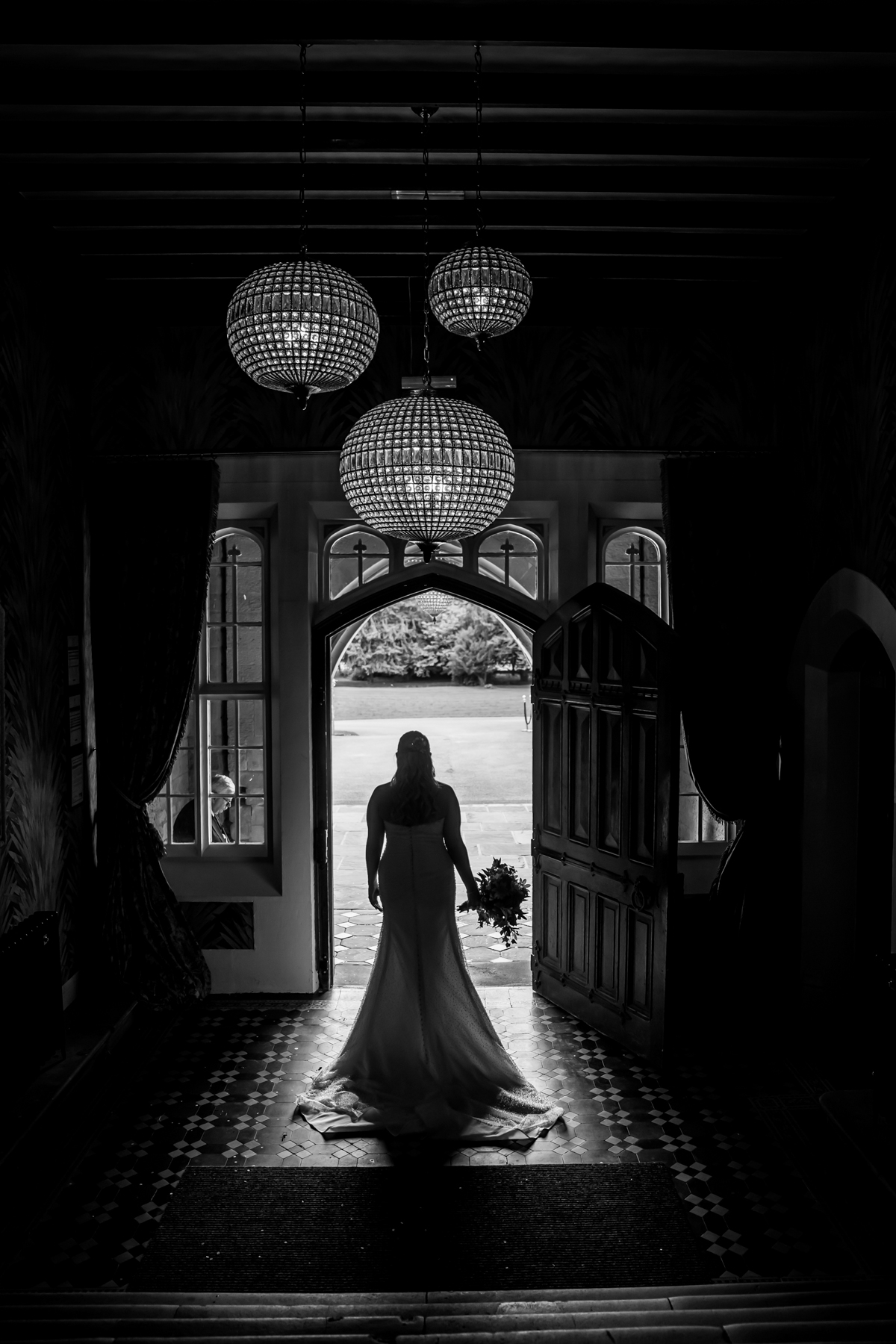 Bride standing in doorway, holding bouquet, silhouette view.