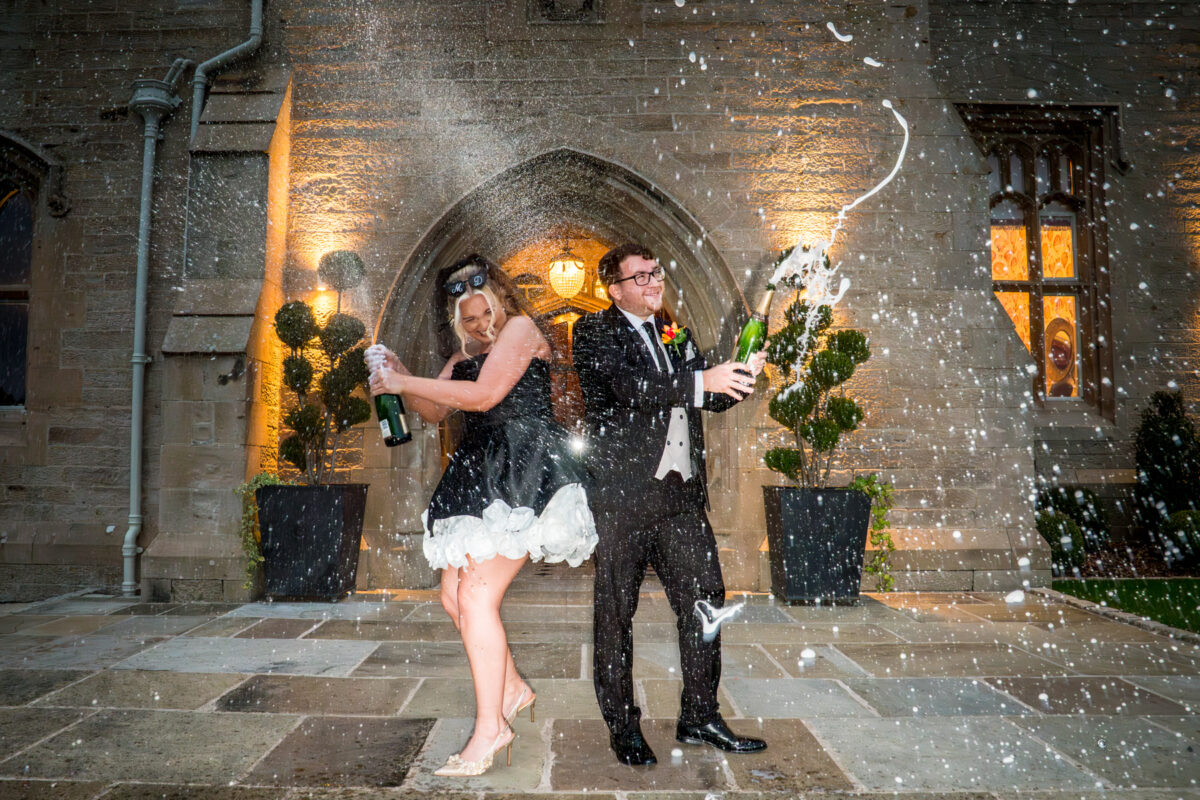Couple celebrating with champagne spray outside church.
