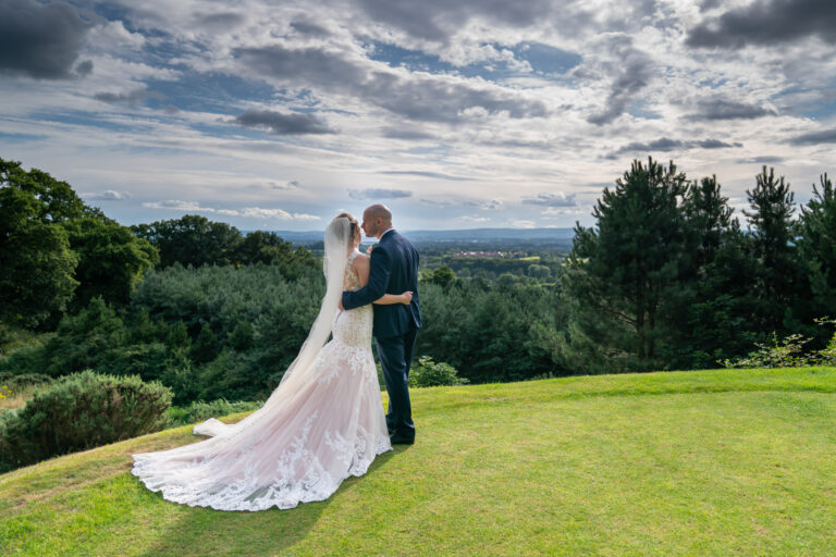 Bride and groom embrace on scenic hilltop.