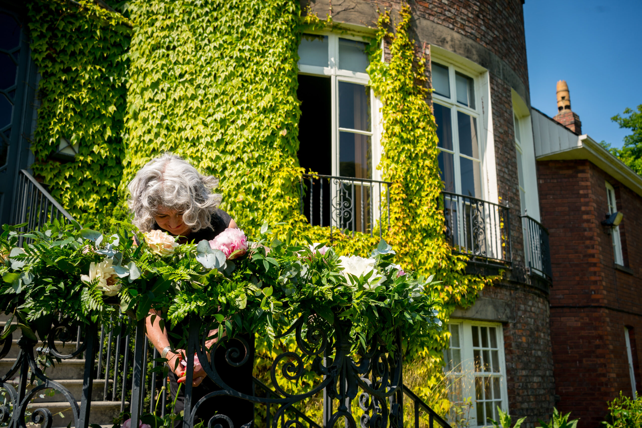 Woman arranging flowers on ivy-covered balcony