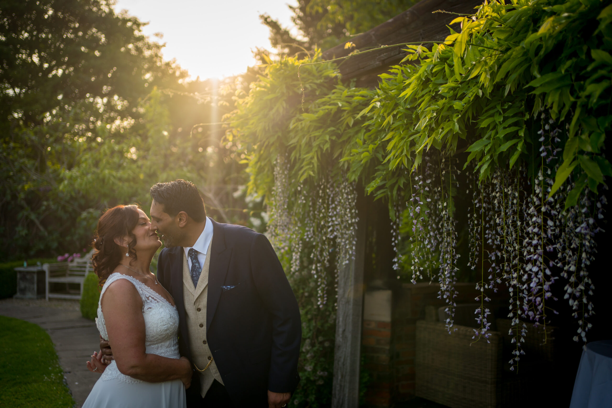 Couple kissing under sunlit pergola.