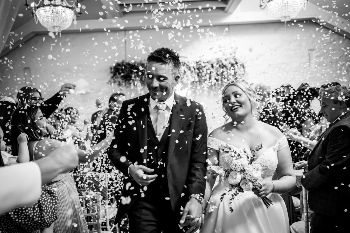 Bride and groom under falling confetti.