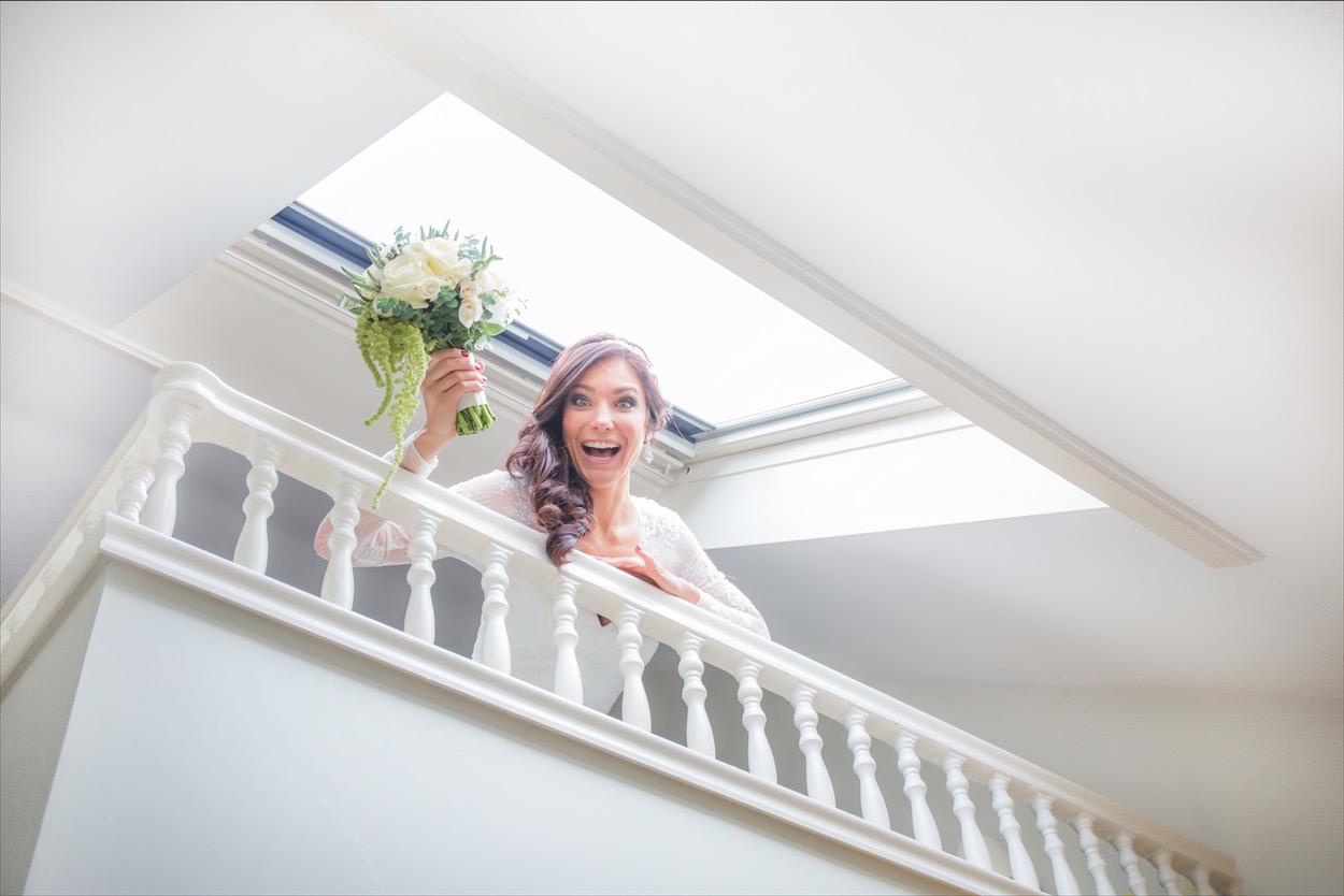 Bride laughing holding bouquet by window