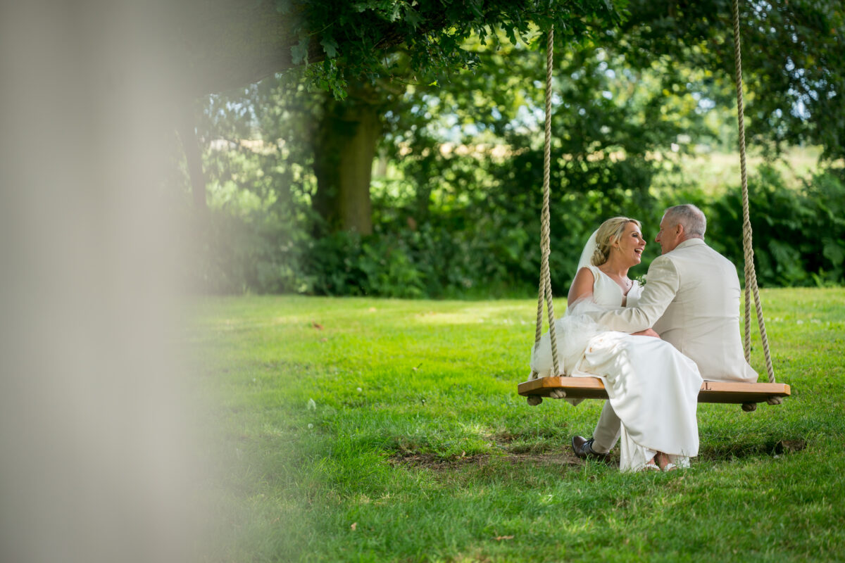 Bride and groom on rustic swing outdoors.