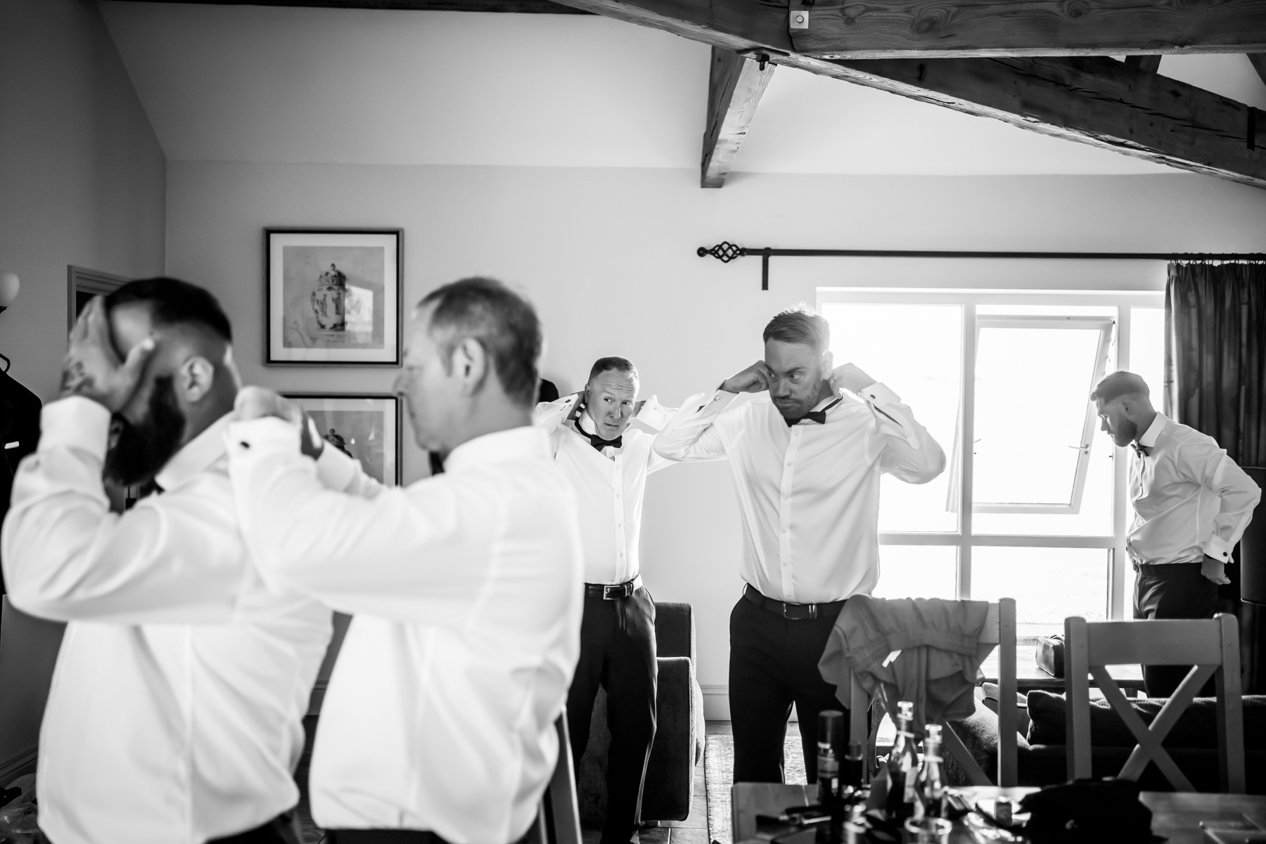 Groomsmen adjusting bow ties in bright room
