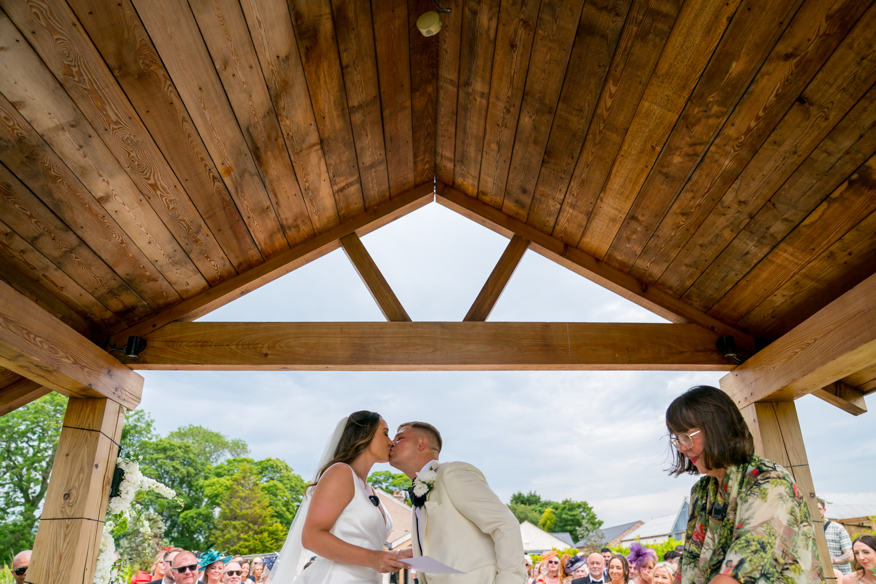 Bride and groom kissing under wooden gazebo