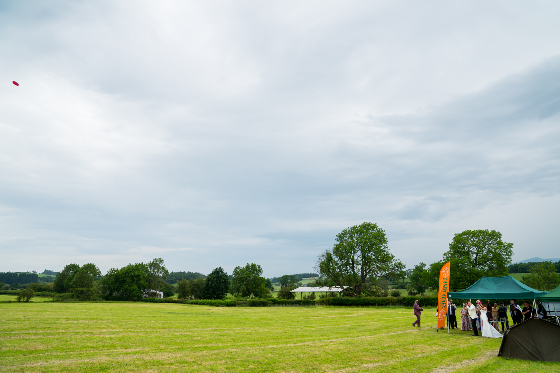 Outdoor wedding party in countryside field with marquee
