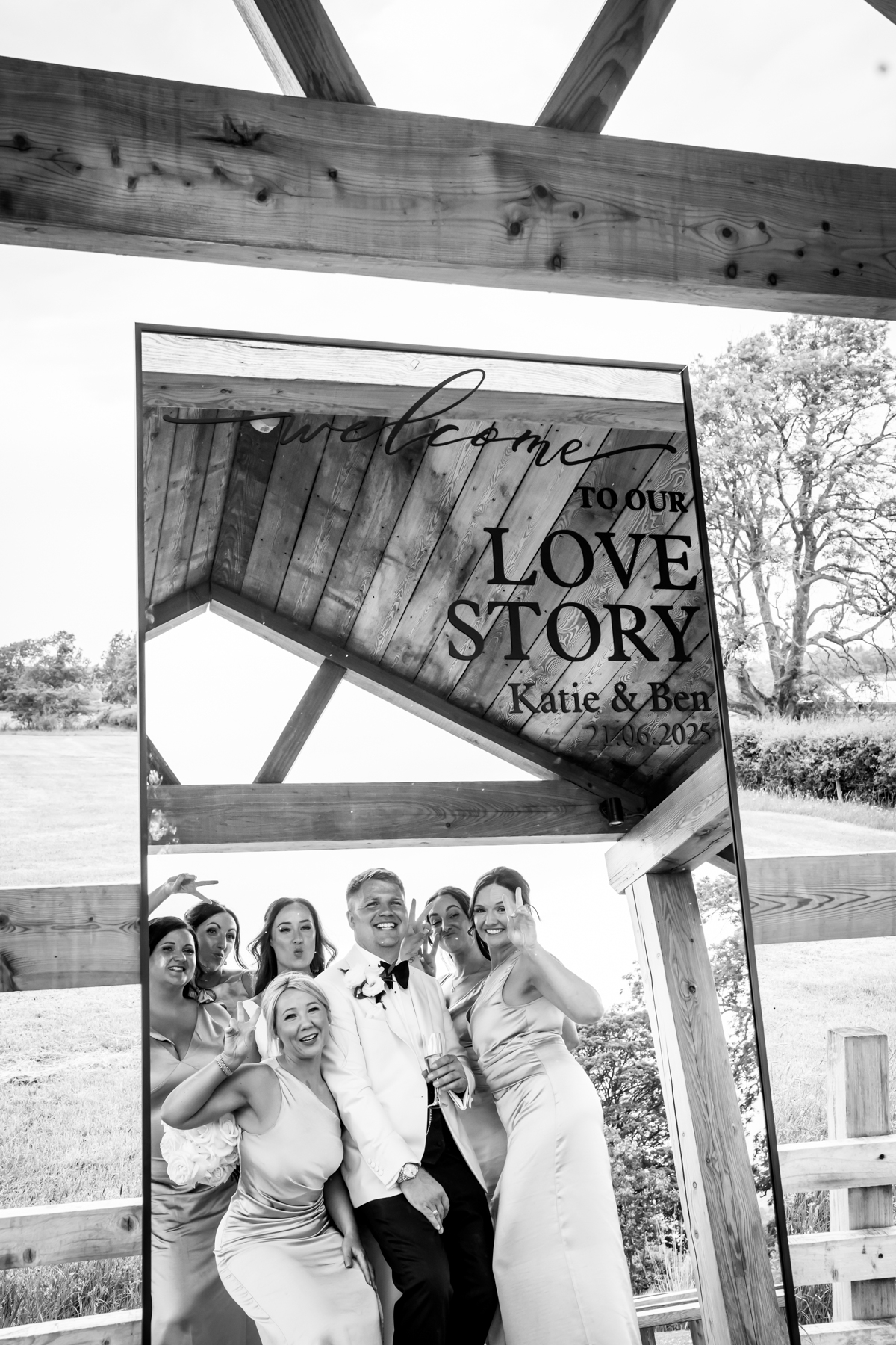 Groom and bridesmaids posing by wedding mirror sign