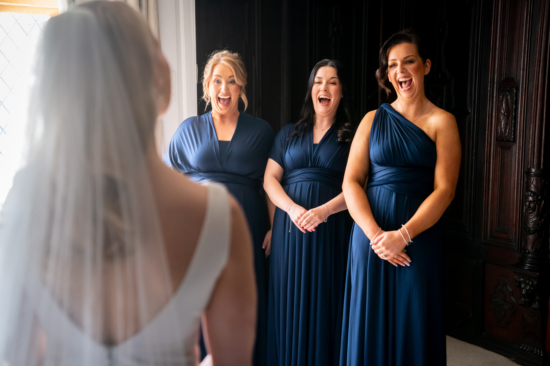 Bridesmaids reacting excitedly to bride in wedding dress