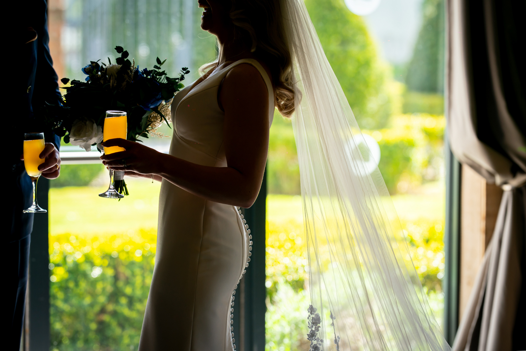 Bride holding champagne by sunlit window