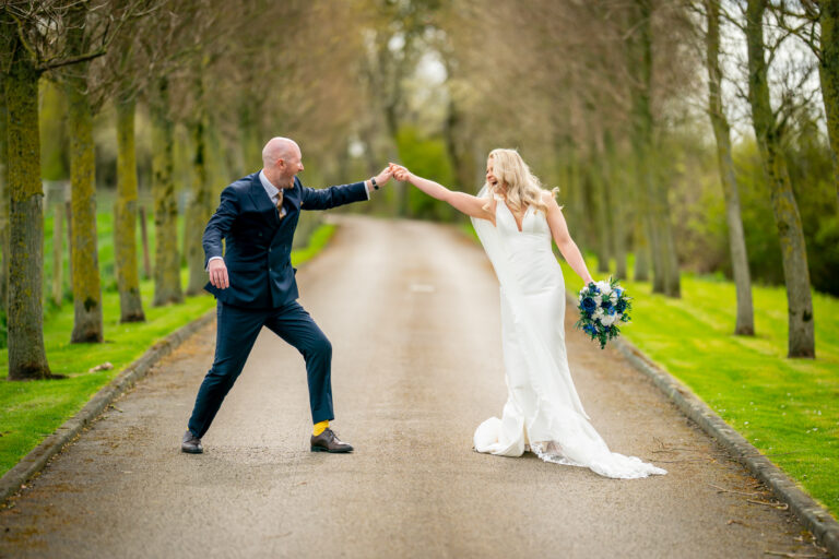 Bride and groom dancing on tree-lined avenue