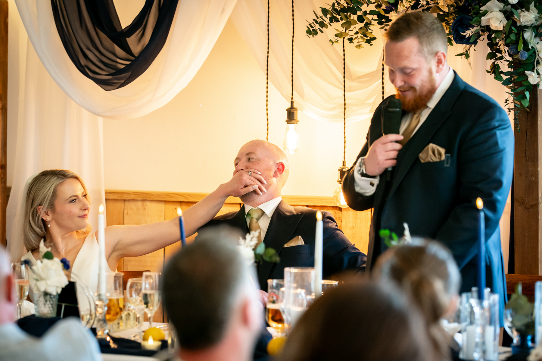Bride playfully covers groom’s mouth during wedding speech
