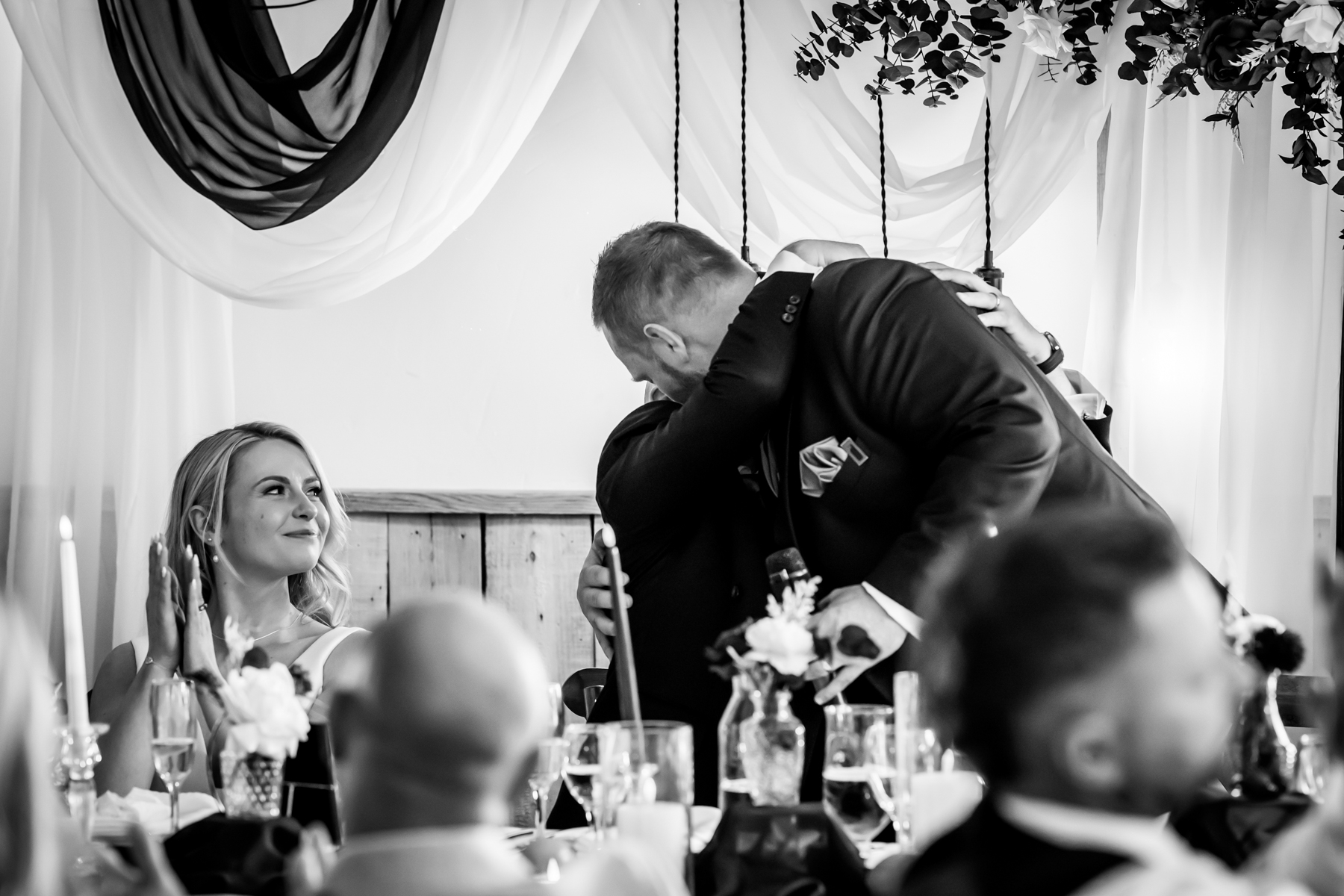 Groom hugging guest as bride applauds at reception