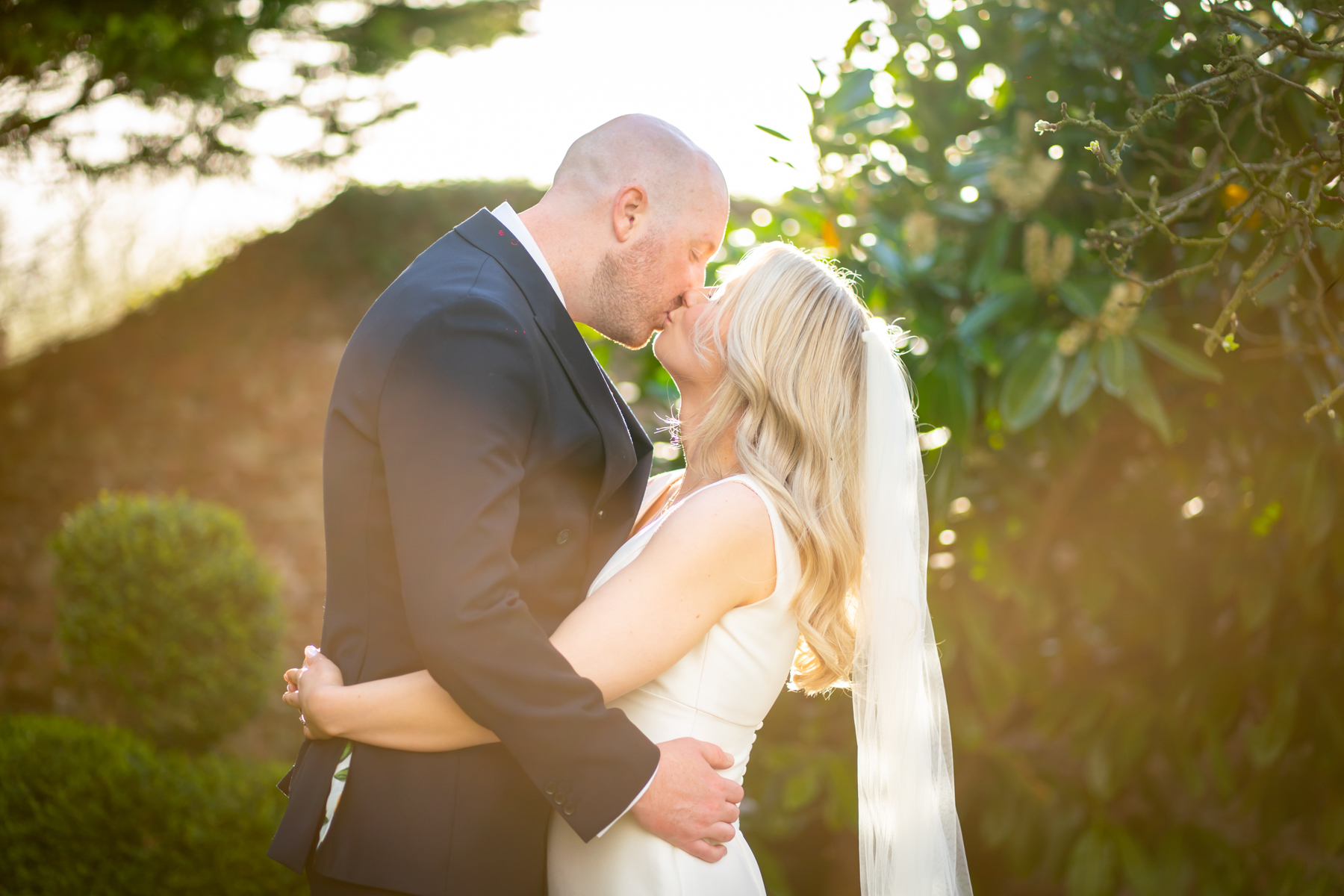 Bride and groom kissing in sunlit garden