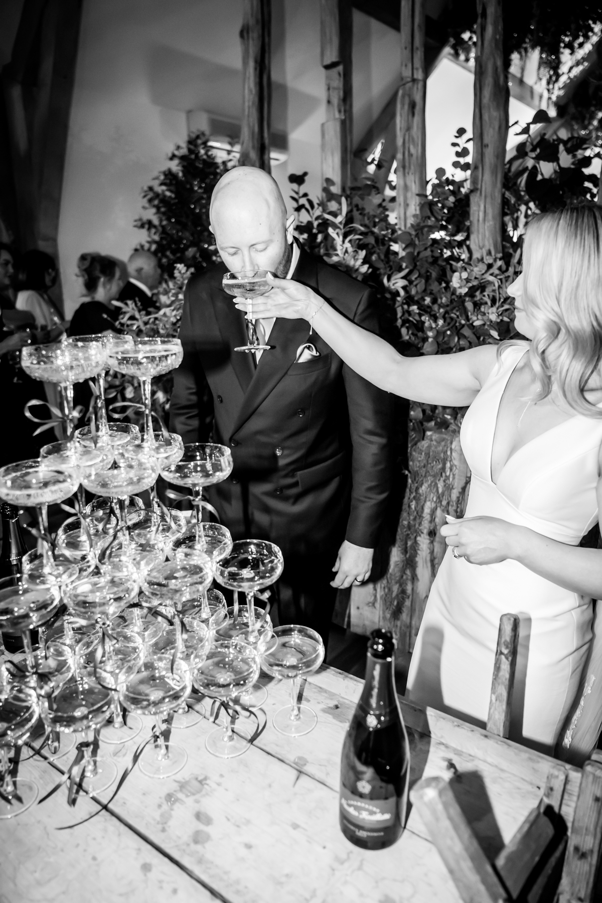 Bride feeding groom champagne beside champagne tower